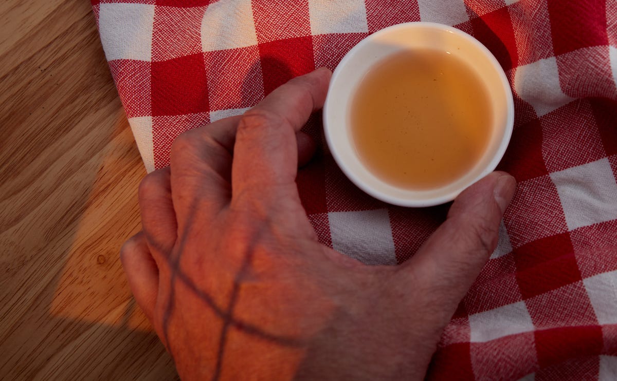 A hand holding a small cup of cider vinegar